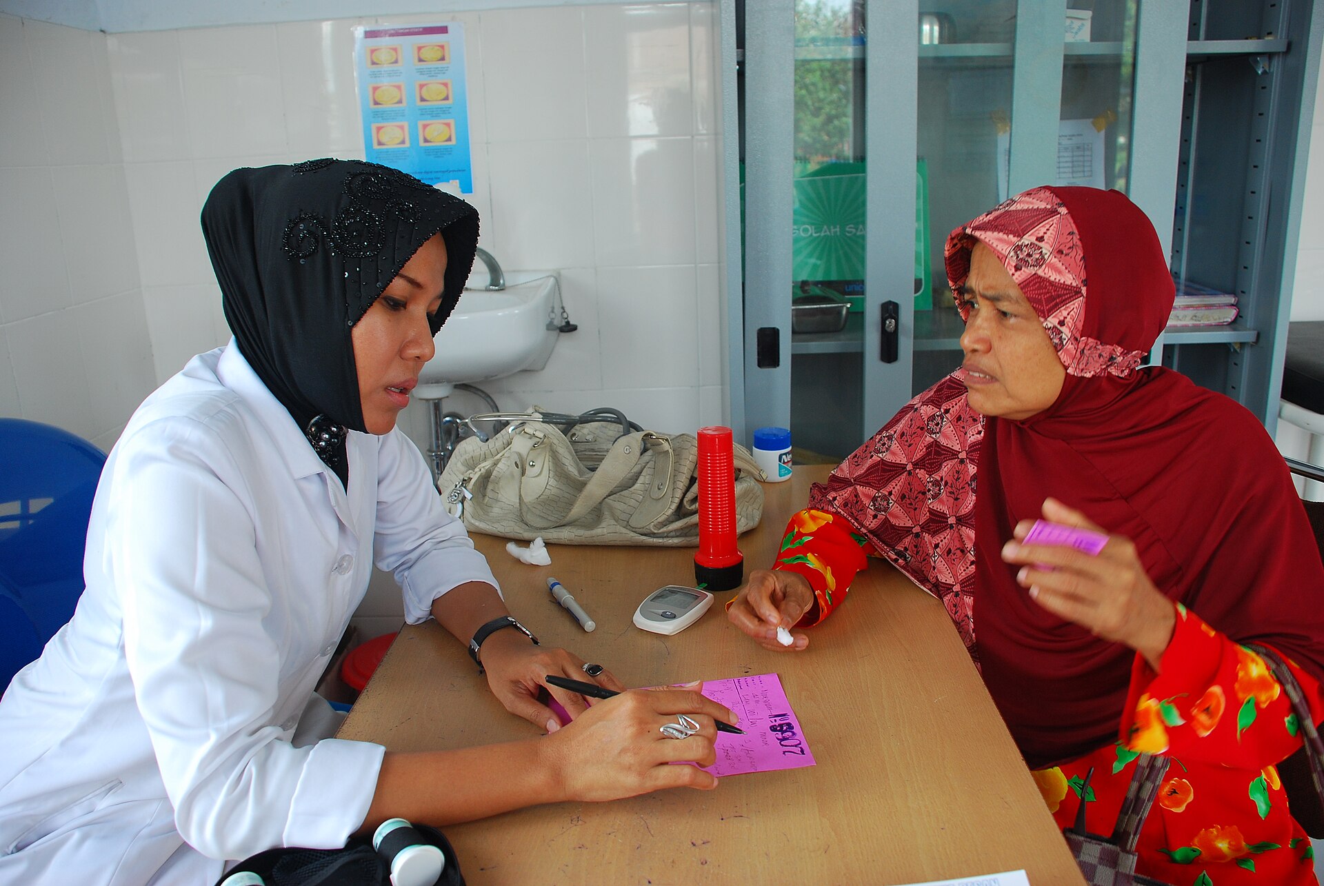 A nurse checking a patient's blood sugar with a glucose meter at an Indonesian community health centre